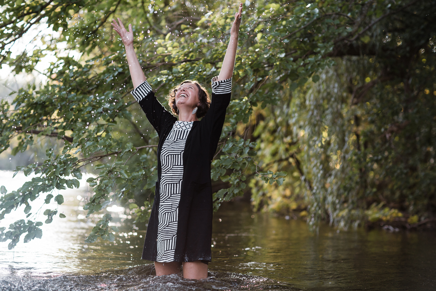 Stephanie Heit river arms up for web Poet Stephanie Heit throws her arms up while wading in a river. Photo by Tamara Wade