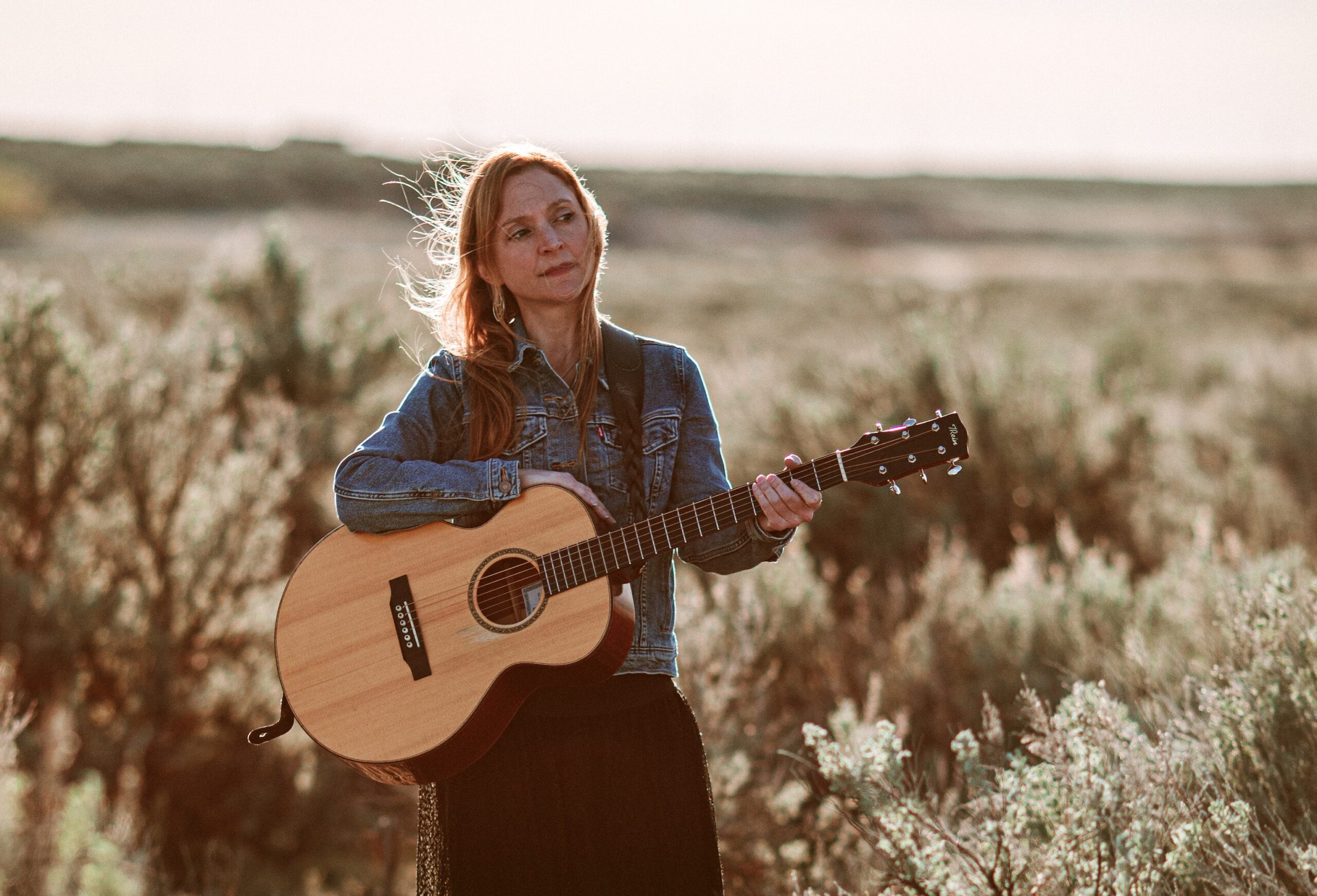 Eilen Jewell holds her acoustic guitar in the desert.